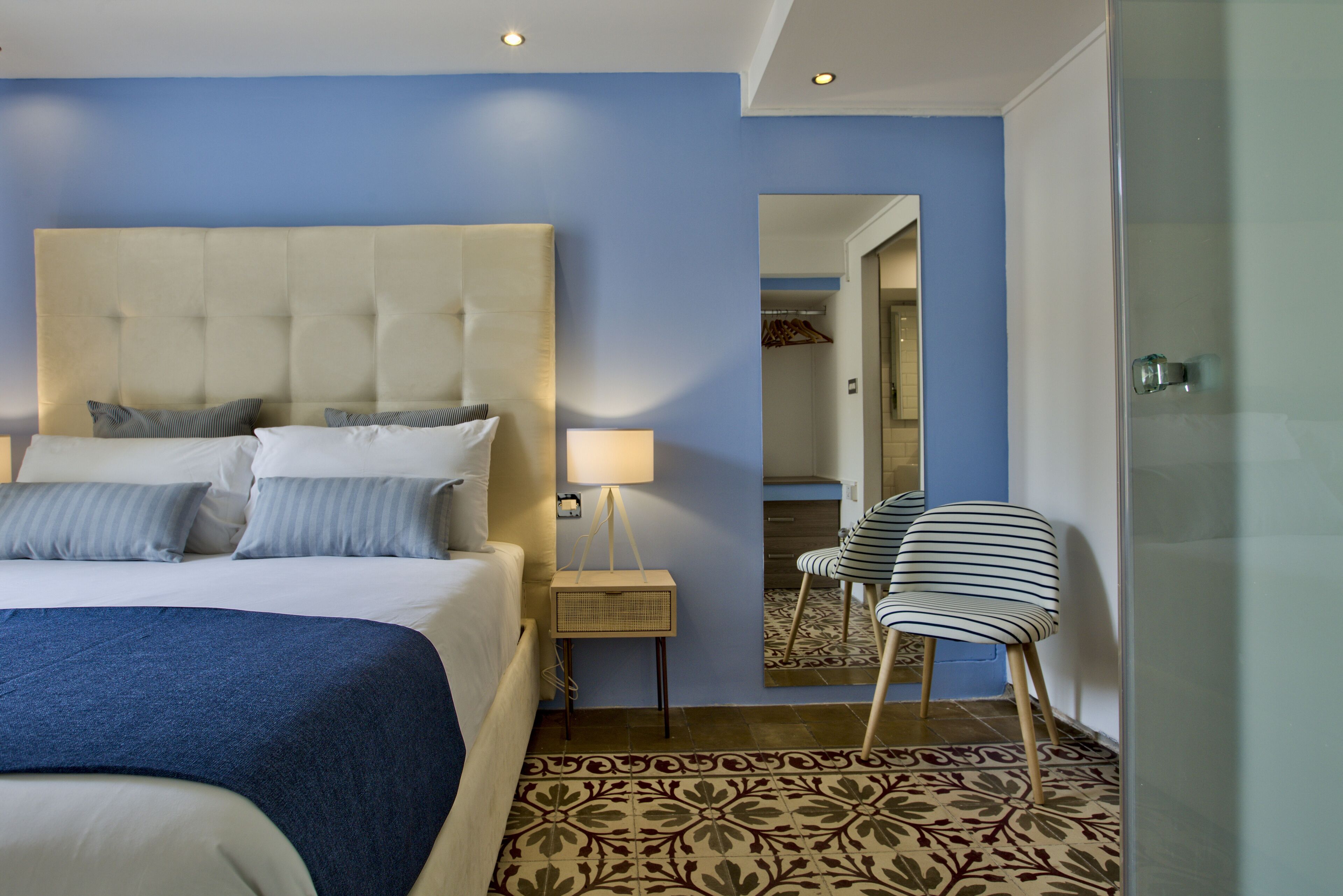 Ein Hotelzimmer mit einem großen Bett, einer Nachttischlampe, einem Spiegel und einem gestreiften Sessel.