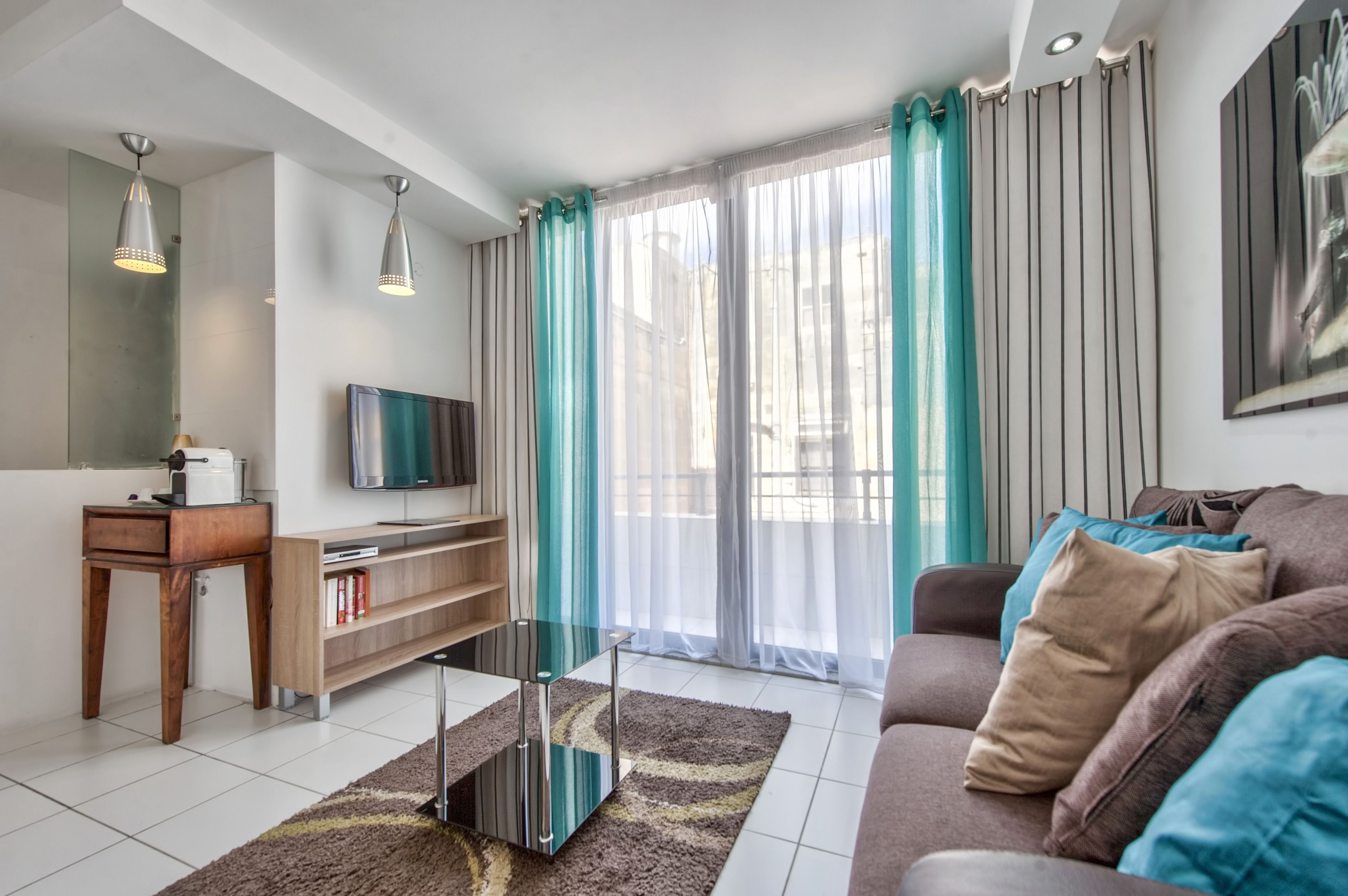 Una sala de estar moderna con sofá, televisor, mesita de madera y una mesa de centro de vidrio.