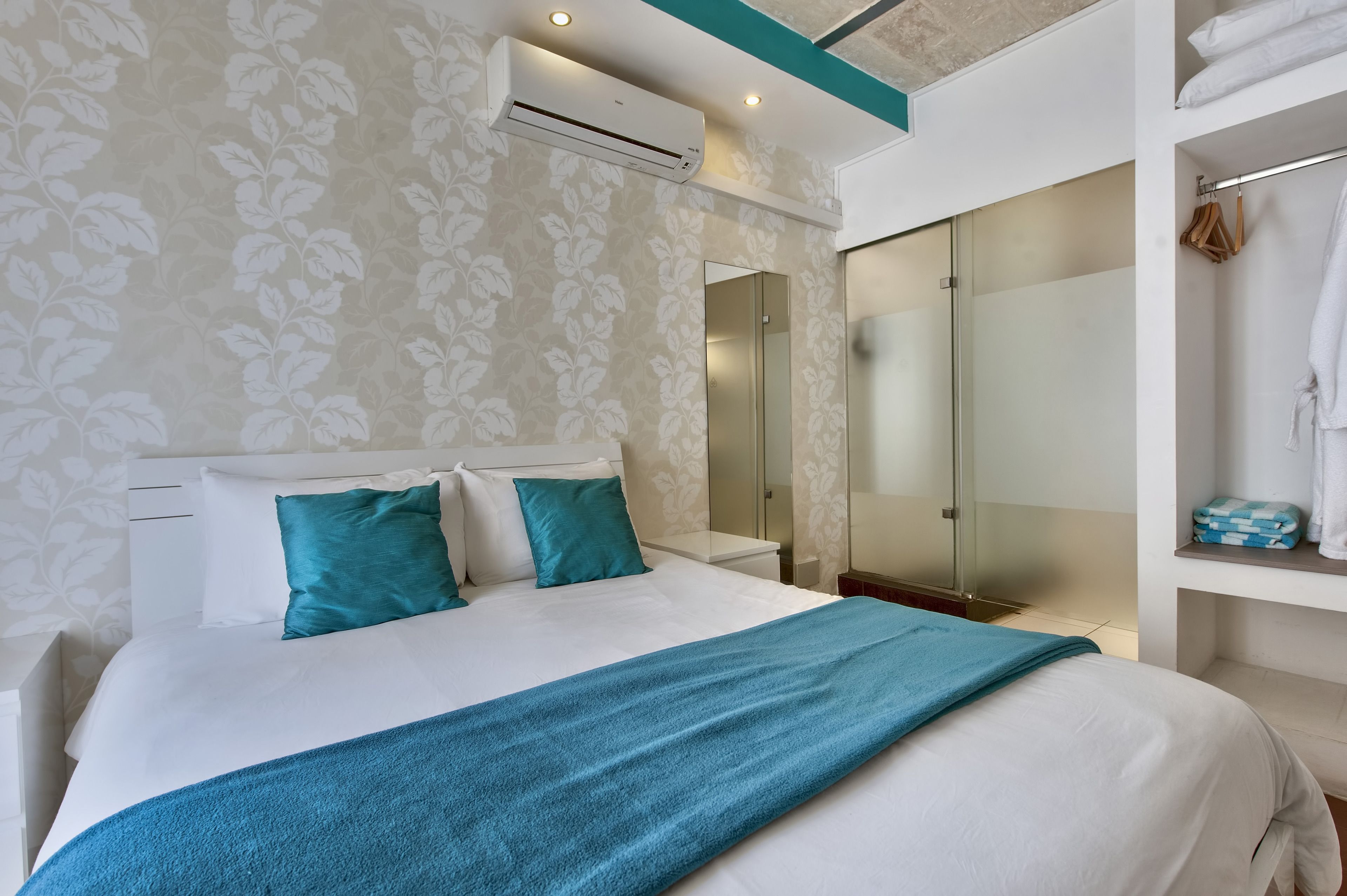 Une chambre moderne avec un grand lit, une douche en verre et une armoire où sont suspendus les vêtements.