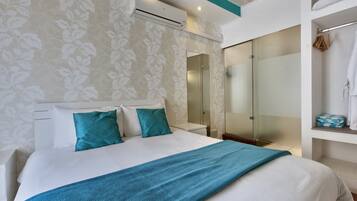 Une chambre moderne avec un grand lit, une douche en verre et une armoire où sont suspendus les vêtements.