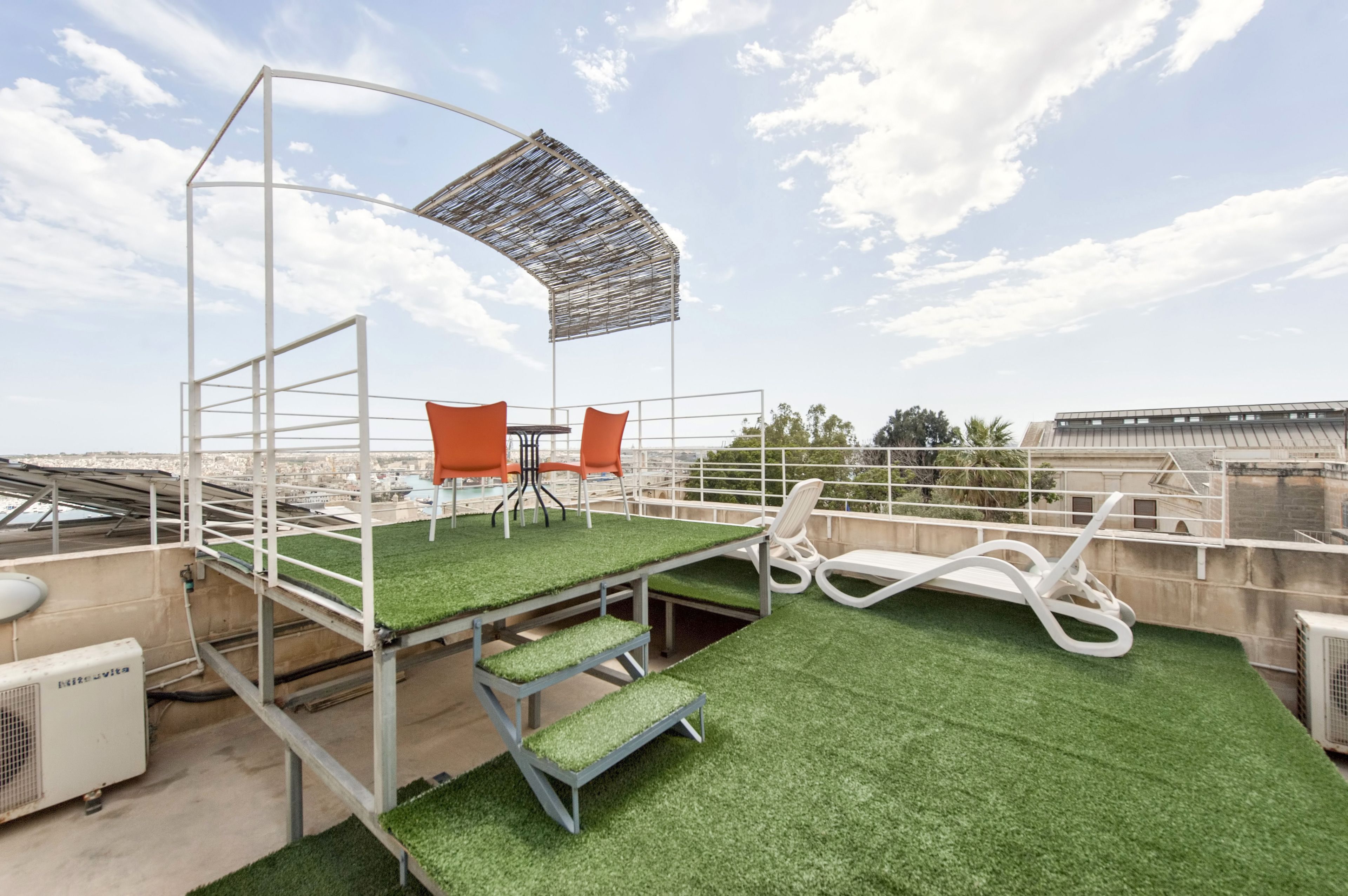 A rooftop terrace with artificial grass, a table with chairs, and a shaded area.