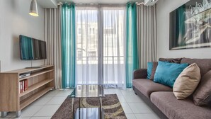 Una sala de estar moderna con sofá, televisor, estantería y un amplio ventanal con cortinas.