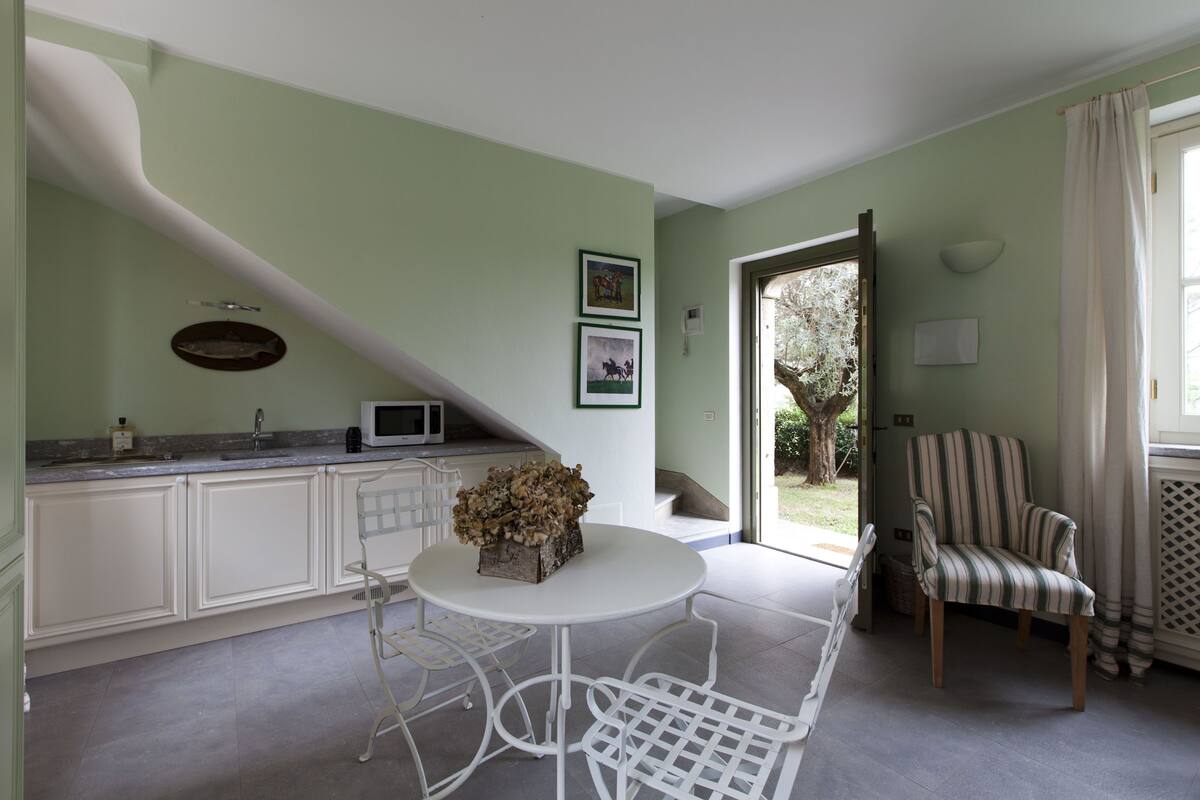 Une cuisine avec des meubles blancs, une table blanche et des chaises, un four à micro-ondes et un vase décoratif.