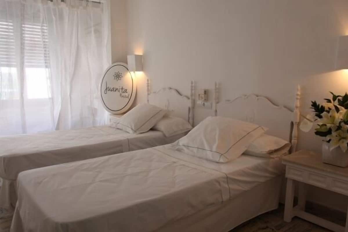 A hotel room with two single beds, a bedside table with a lamp, and a wall-mounted light fixture.