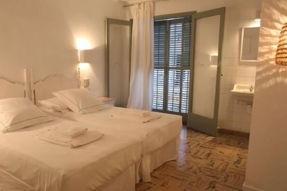 A hotel room with two beds, a bathroom with a sink, and a view of the outside through a door.