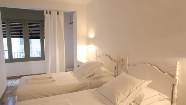 Un dormitorio con dos camas, una ventana con contraventanas y una mesita de noche con lámpara.