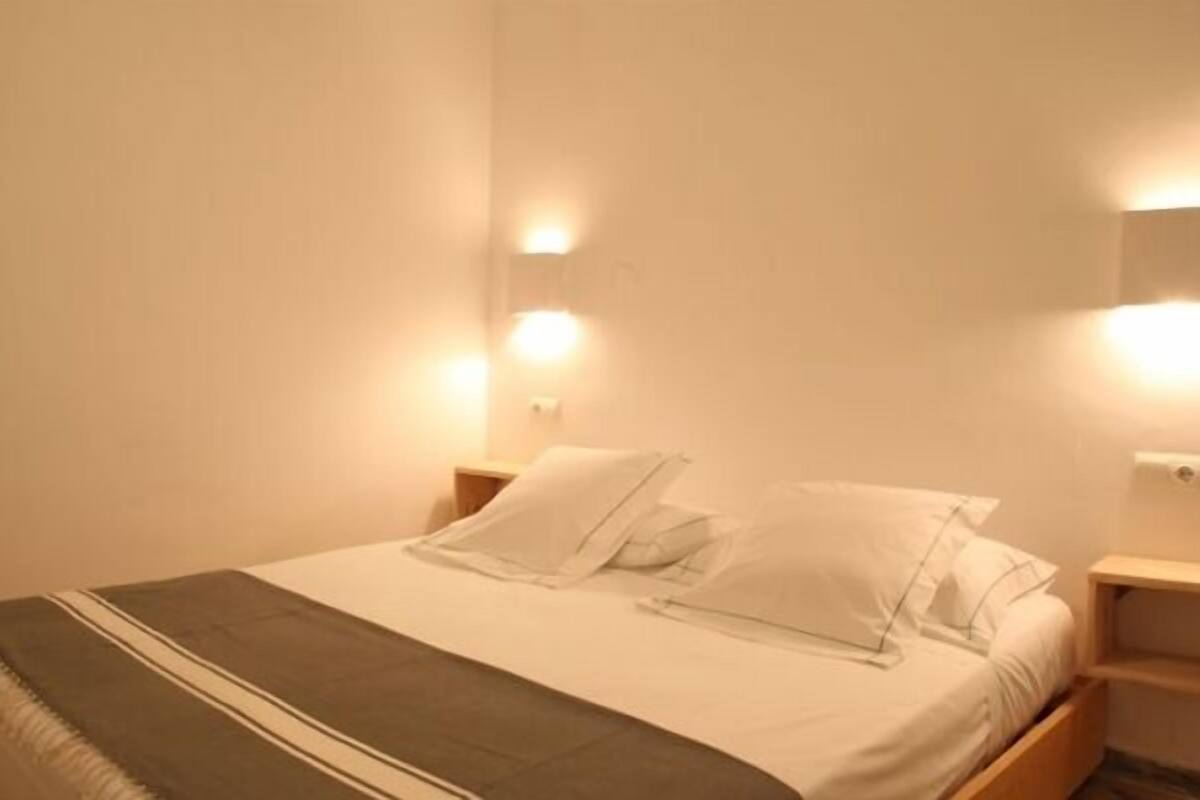 A neatly made bed with white linens and pillows, a gray throw blanket, and bedside tables with wall-mounted lights.