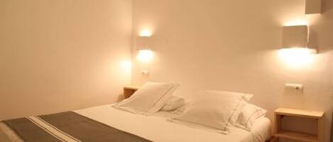 A neatly made bed with white linens and pillows, a gray throw blanket, and bedside tables with wall-mounted lights.