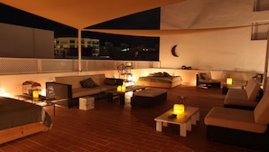 Un salón en la azotea con piso de ladrillo, varias zonas de estar e iluminación ambiental.