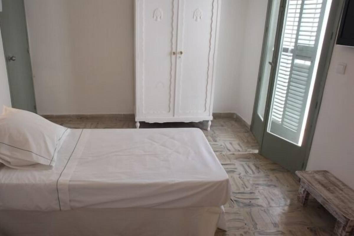 A bedroom with a bed, a wardrobe, a bench, and a window with blinds.