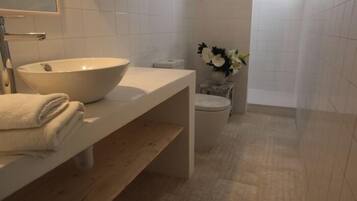 A modern bathroom with a large white sink, a toilet, and a shower area.