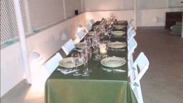 Una larga mesa dispuesta para una comida bajo una estructura cubierta, con sillas blancas.