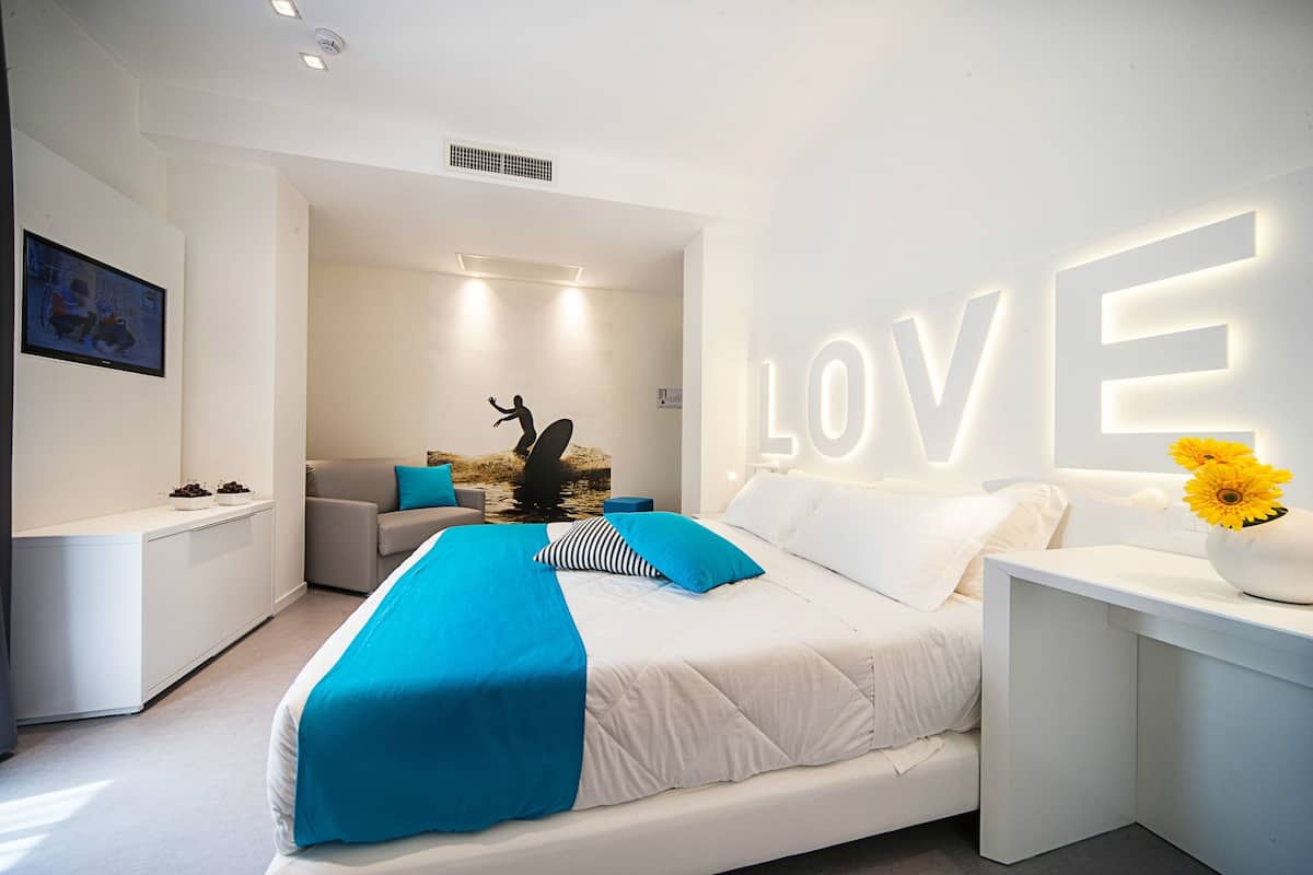 A modern bedroom with a large bed, a sofa, and a desk. The word "LOVE" is prominently displayed on the wall.