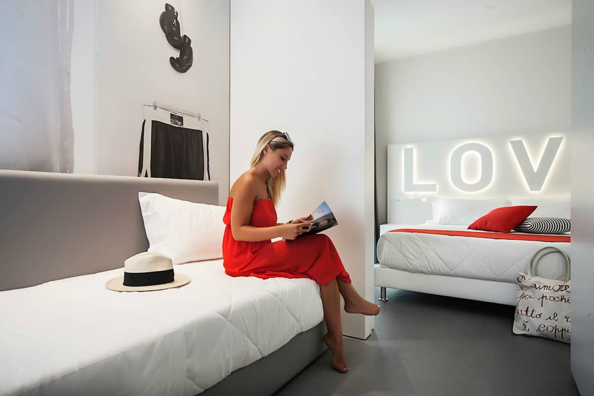 A modern hotel room with a bed, a reading area, and a wall with the word "LOV" illuminated.