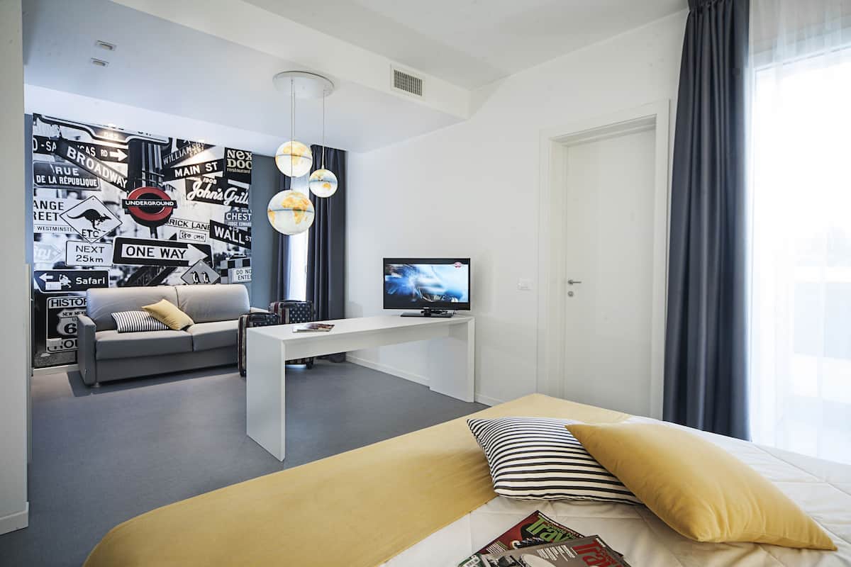A modern hotel room with a bed, a sofa, a desk, and a television.