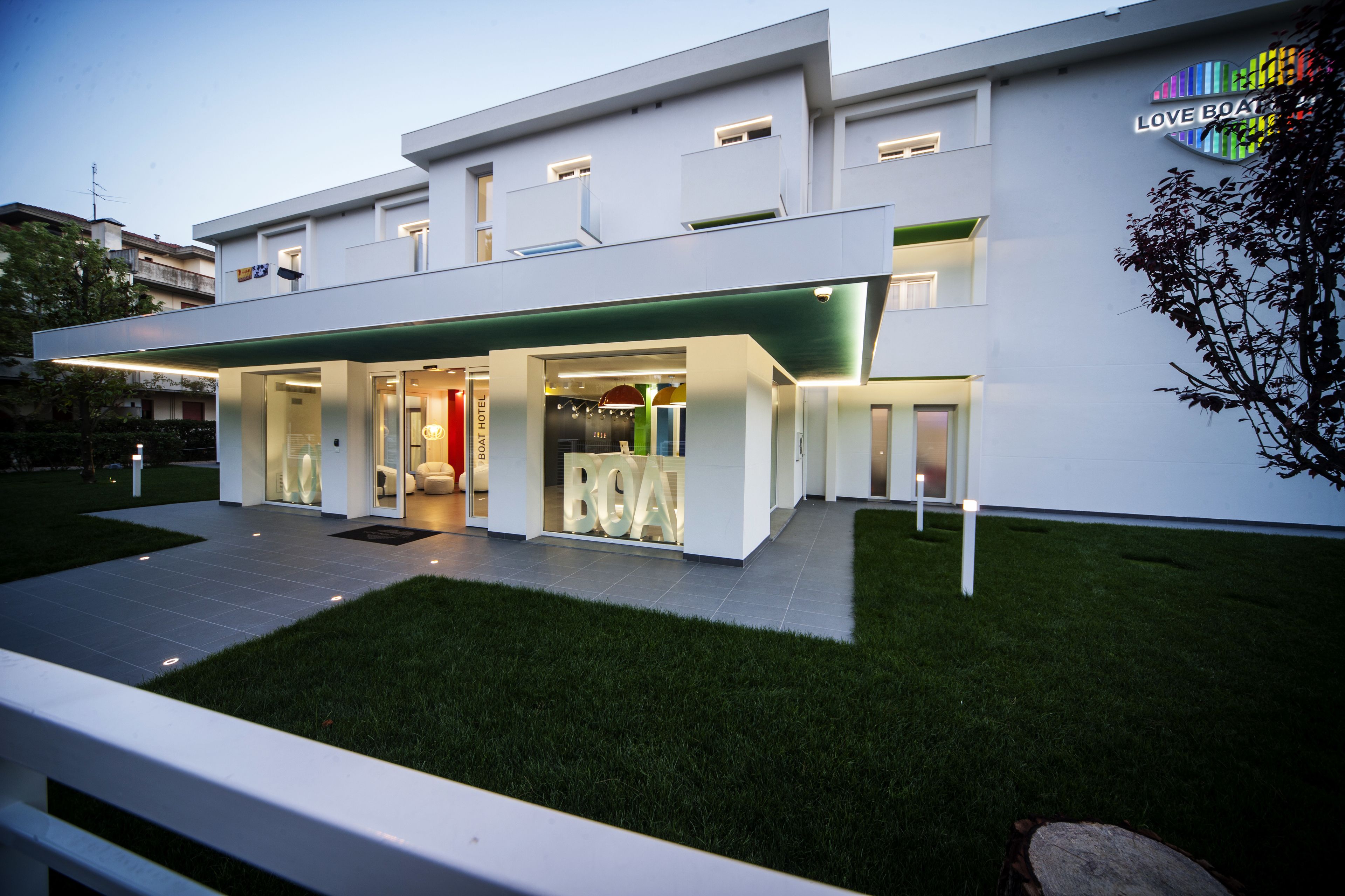 A modern hotel with a glass facade, a green awning, and a sign reading "LOVE BOAT".