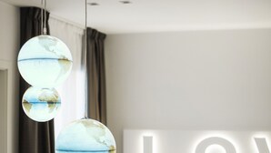 A modern hotel room with a bed, a bedside table, and a globe-shaped hanging light fixture. - Love Boat (Riccione)