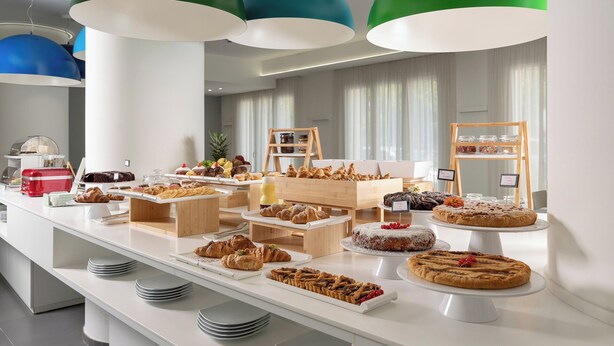 A buffet with various pastries and desserts, including cakes and pastries, arranged on a white table with a modern design. - Love Boat (Riccione)