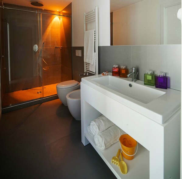 A modern bathroom with a glass-enclosed shower, a toilet, and a large sink with toiletries. - Love Boat (Riccione)