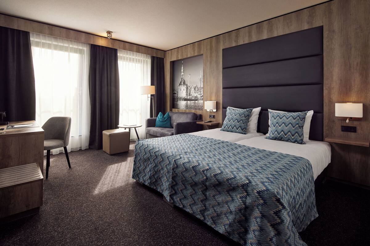 Ein Hotelzimmer mit einem großen Bett, einem Schreibtisch, einem Stuhl, einem kleinen Tisch und einem an der Wand befestigten Fernseher.
