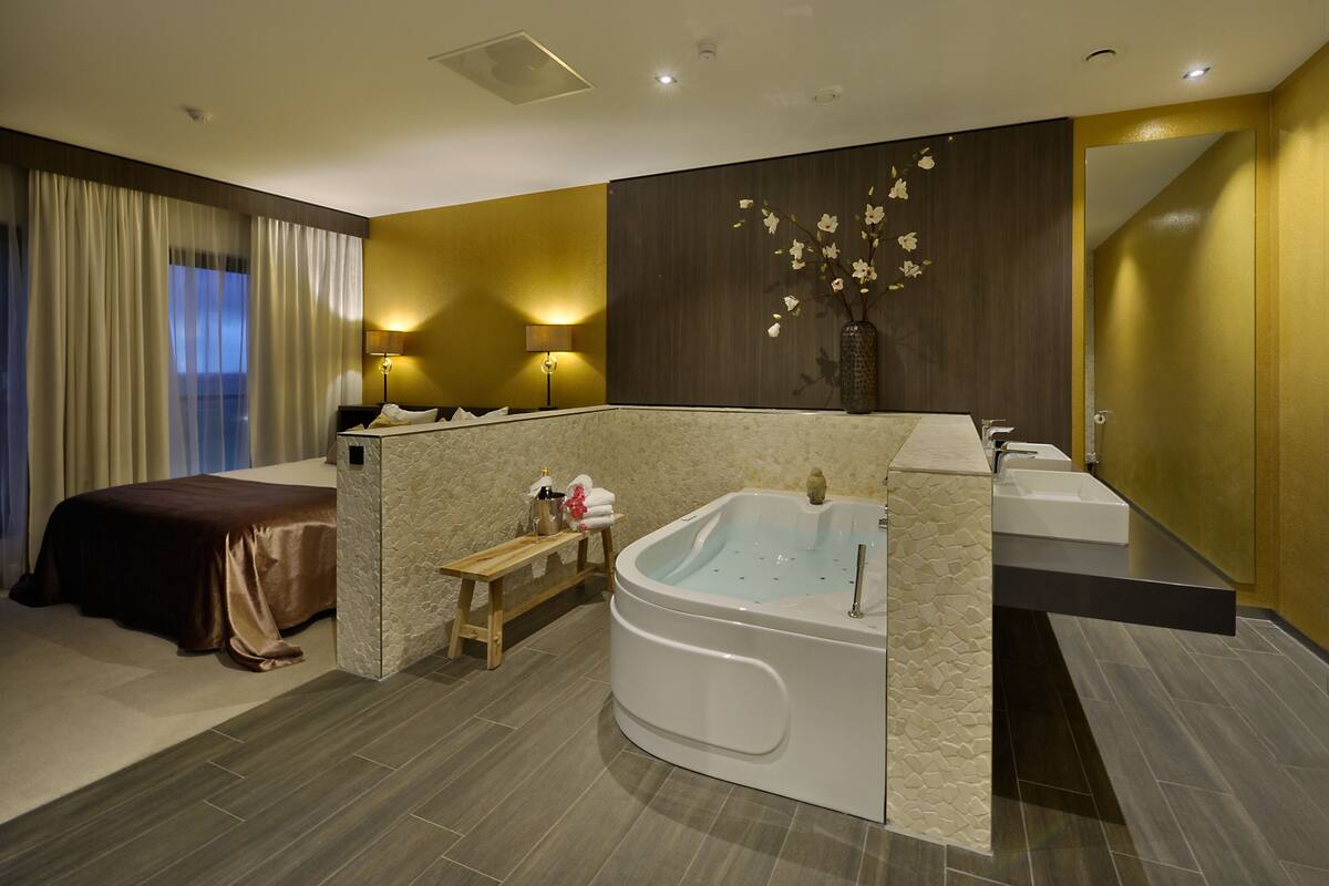 Ein modernes Hotelzimmer mit einem großen Bett, einem separaten Badebereich, einer Badewanne und einem Schminktisch mit Spiegel.