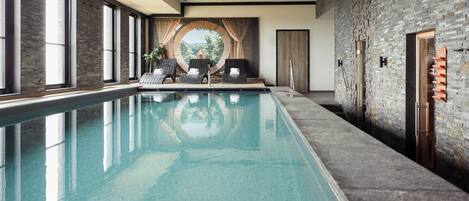 An indoor swimming pool with a stone wall and large windows.