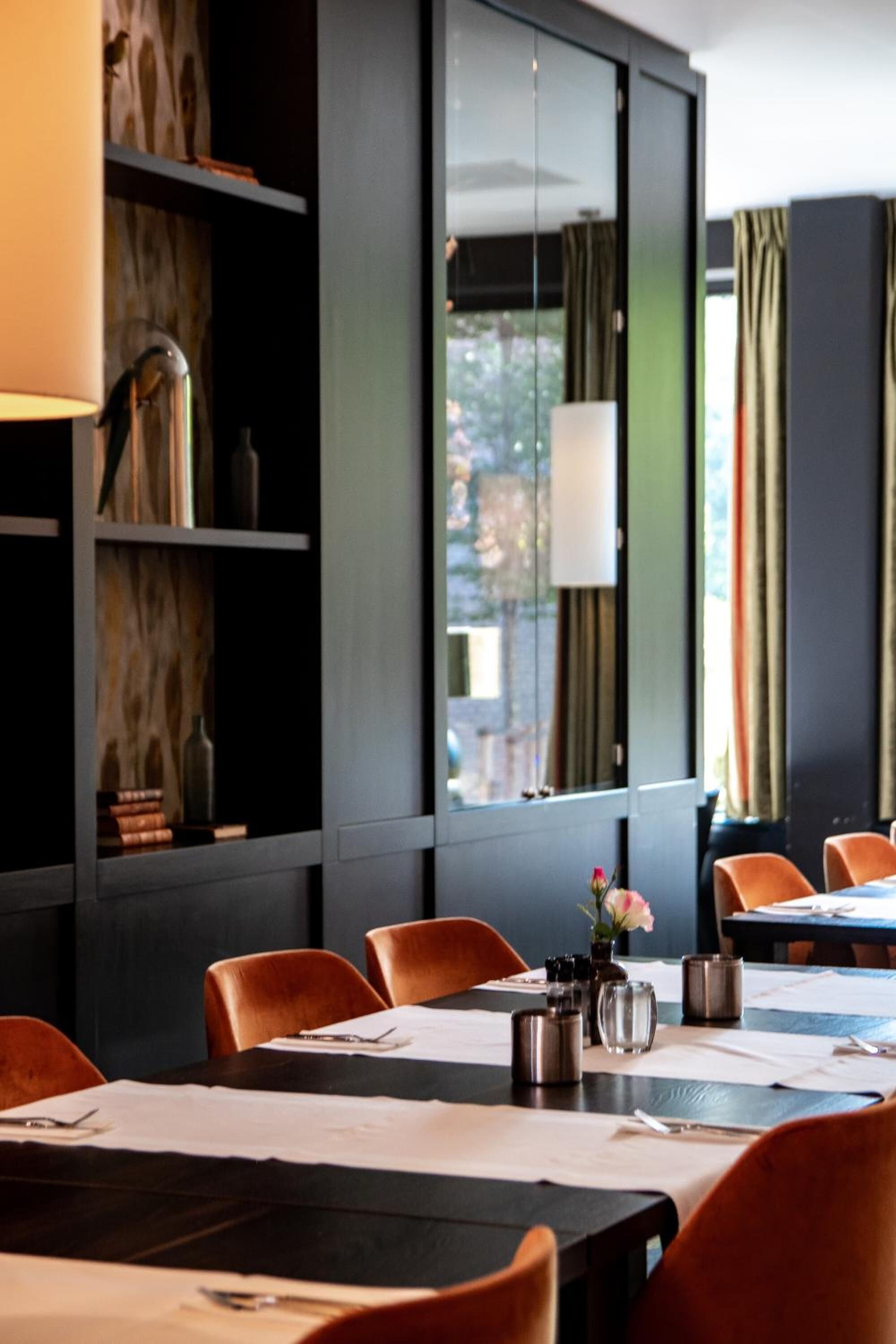 Un comedor moderno con estanterías de madera, un amplio ventanal con cortinas y sillas anaranjadas.