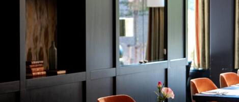 Un comedor moderno con estanterías de madera, un amplio ventanal con cortinas y sillas anaranjadas.