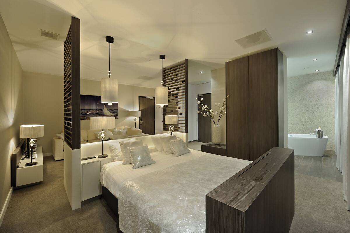 Ein modernes Schlafzimmer mit einem großen Bett, Nachttischen, einem kleinen Schreibtisch, einem Spiegel und einer eingebauten Bank.