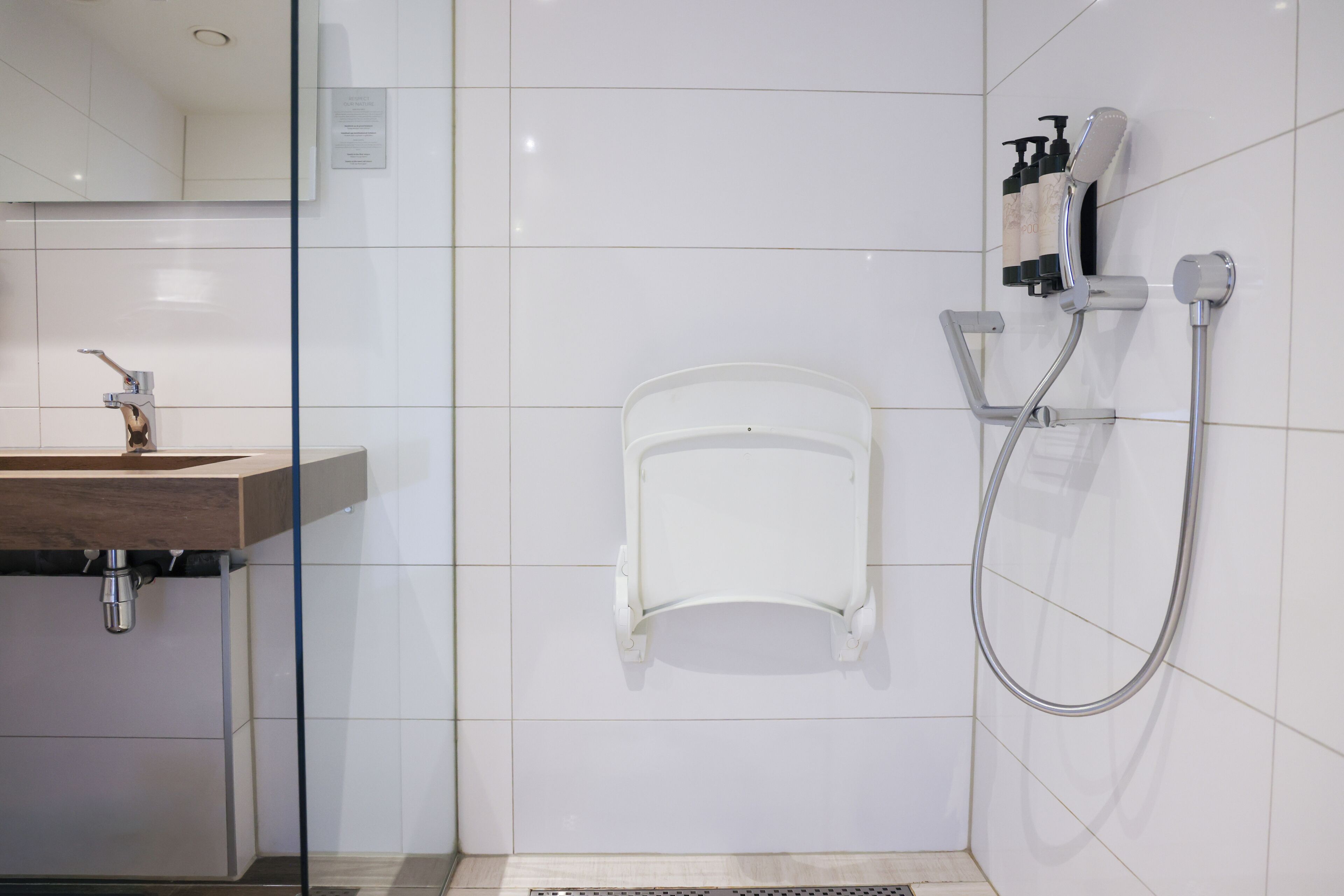 A modern bathroom with a sink, mirror, shower, and toiletries.