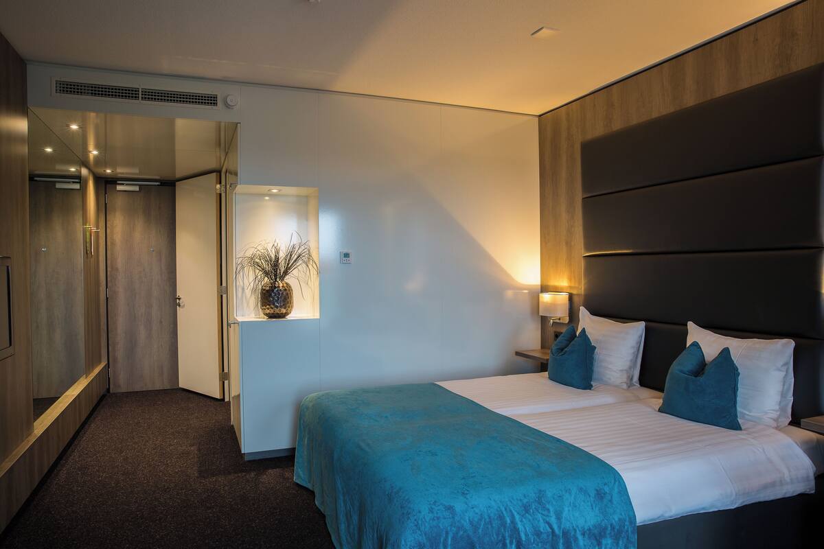 Ein Hotelzimmer mit einem Bett, Nachttischen, einem Spiegel, einer Tür und einer Wandleuchte.