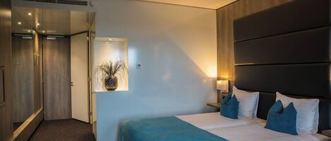 A hotel room with a bed, bedside tables, a mirror, a door, and a wall-mounted light fixture.