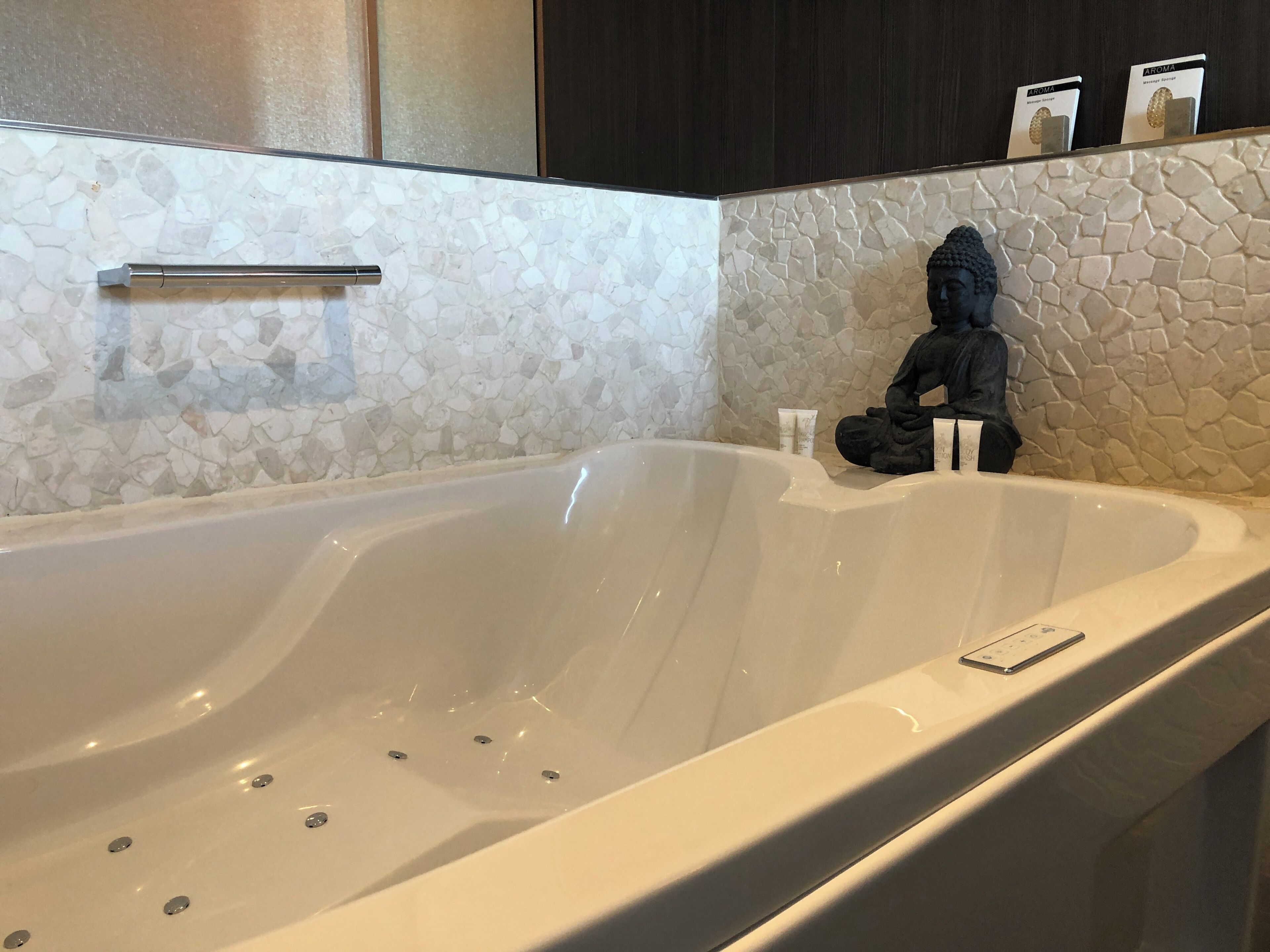 A modern bathroom with a large bathtub, a stone mosaic wall, and a statue.