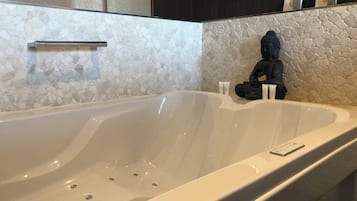 A modern bathroom with a large bathtub, a stone mosaic wall, and a statue.