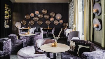 Un interior moderno con mesas redondas y sillas tapizadas de color morado, una pared oscura con arte mural circular y una ventana con cortinas.