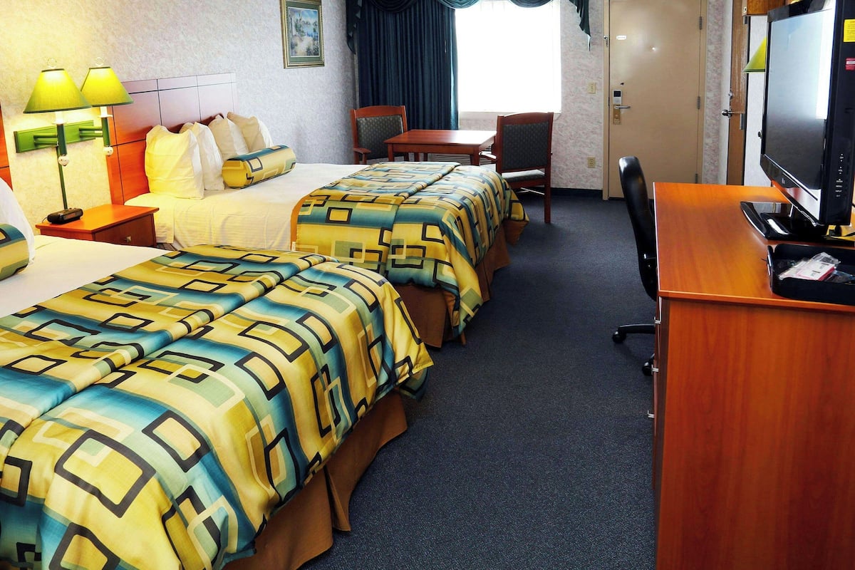 Habitación de hotel con dos camas, un escritorio, televisión y ventana con cortinas.
