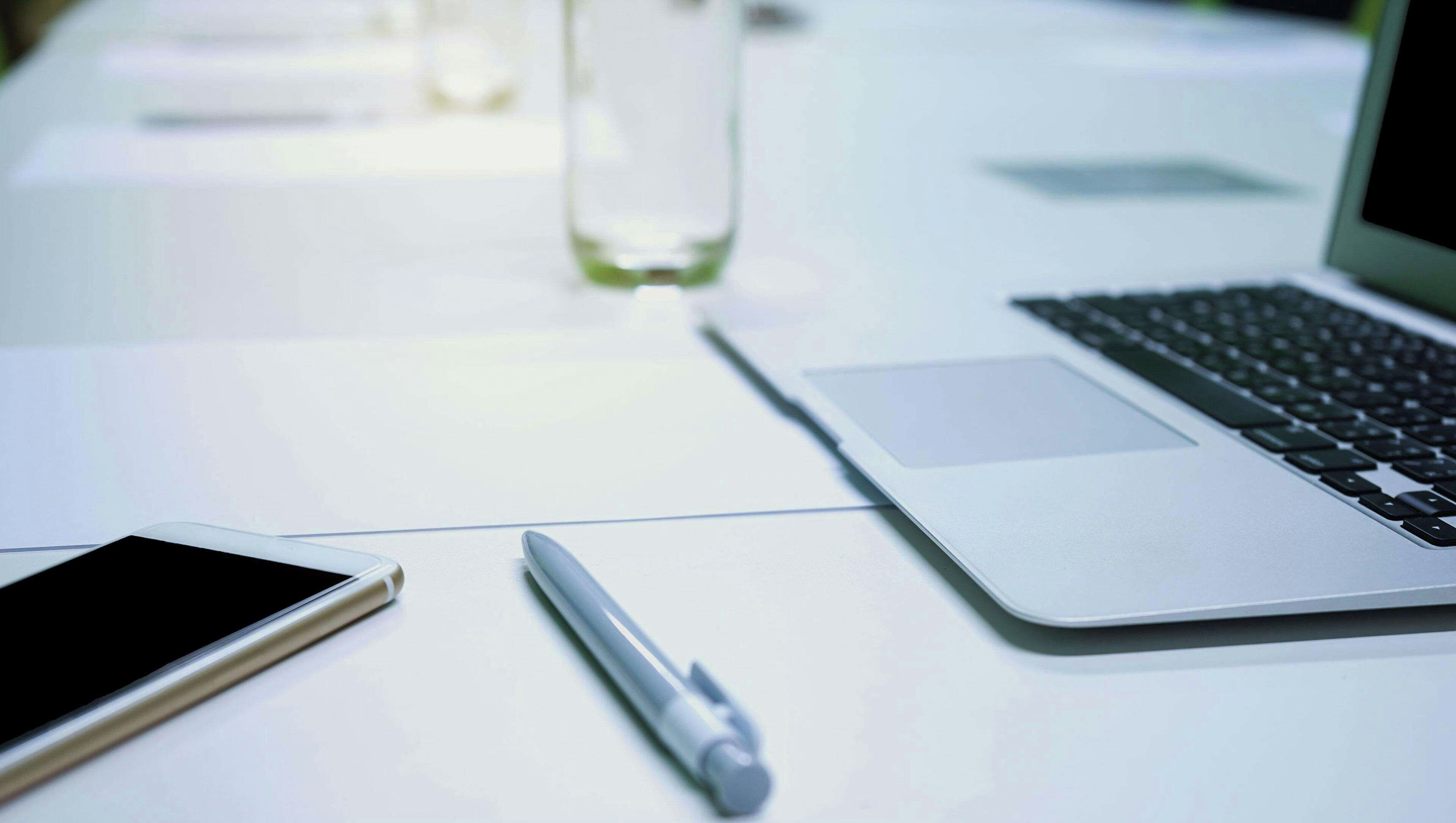 A laptop, a smartphone, and a pen on a white table.