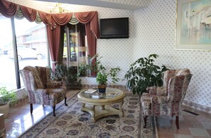A living room with patterned armchairs, a glass coffee table, and a TV mounted on the wall.