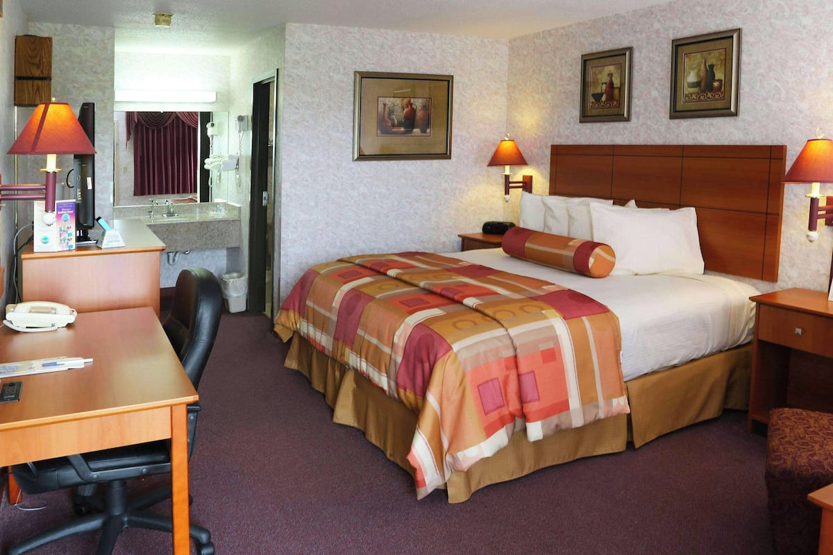 Habitación de hotel con cama, dos lámparas de noche, un escritorio con teléfono, una silla y una mesita.
