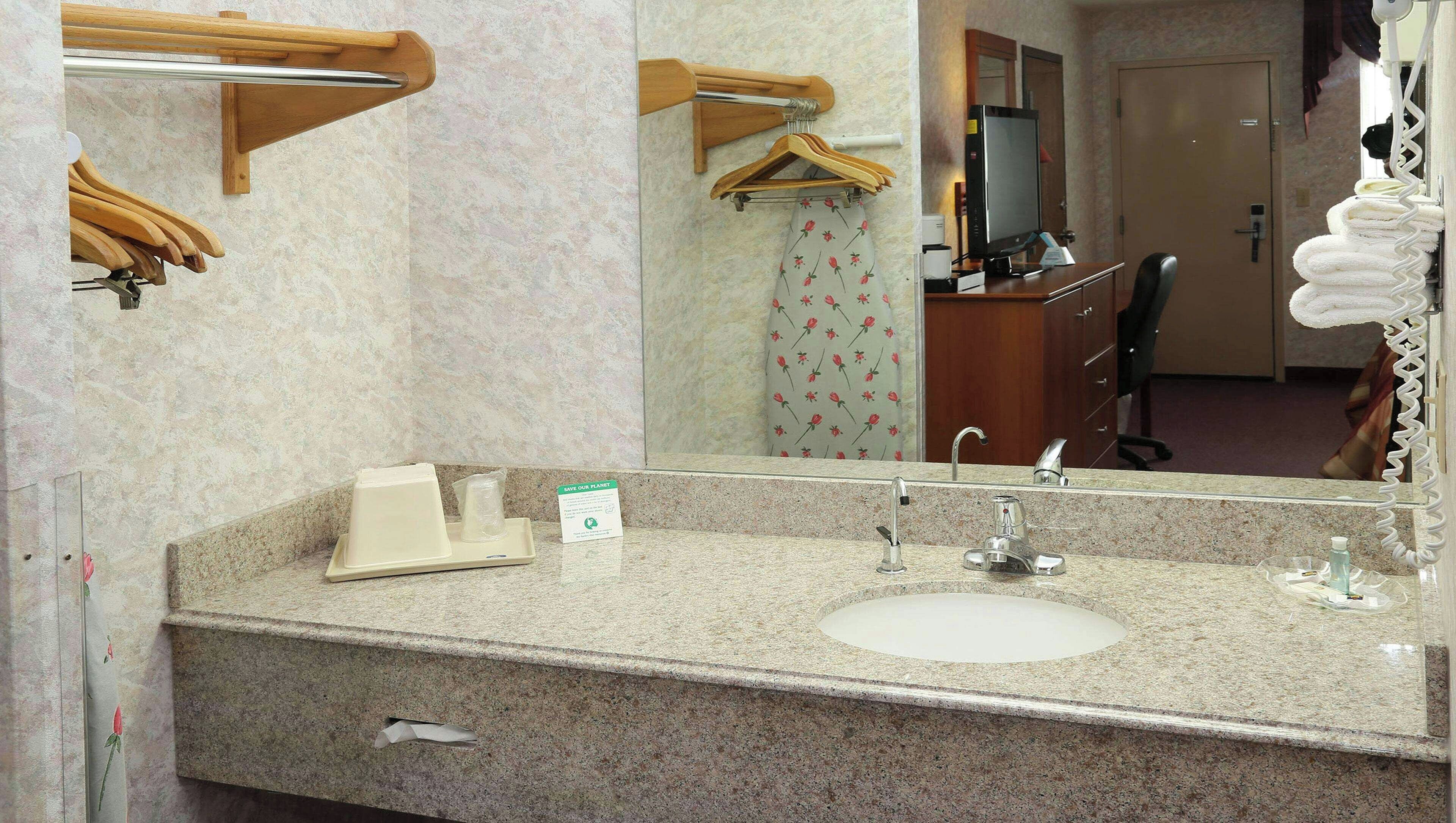 Uma casa de banho com bancada de granito, uma pia, um espelho, um porta-toalhas e uma cortina de chuveiro com padrão floral.