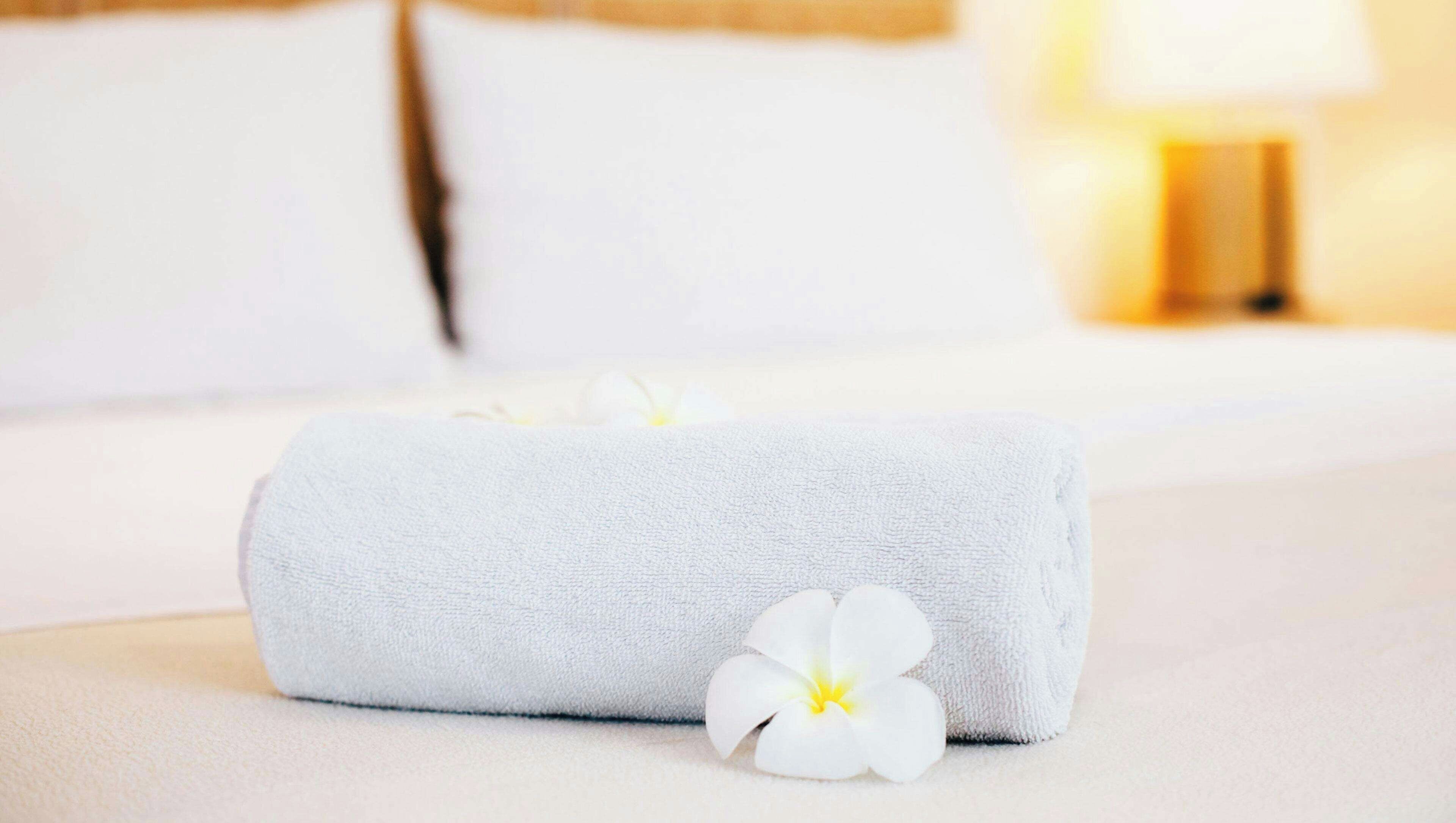 Une serviette blanche, soigneusement pliée, avec une fleur blanche posée sur un lit.