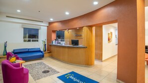 A reception area with a blue sofa, a wooden reception desk, and a blue doormat with the logo 'Mágico'.