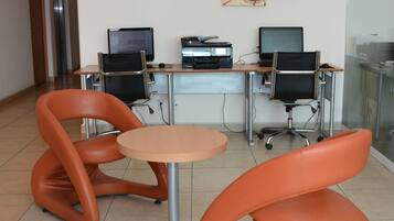 Um espaço de escritório moderno com duas cadeiras ergonômicas laranja, uma mesa redonda e dois computadores de mesa.