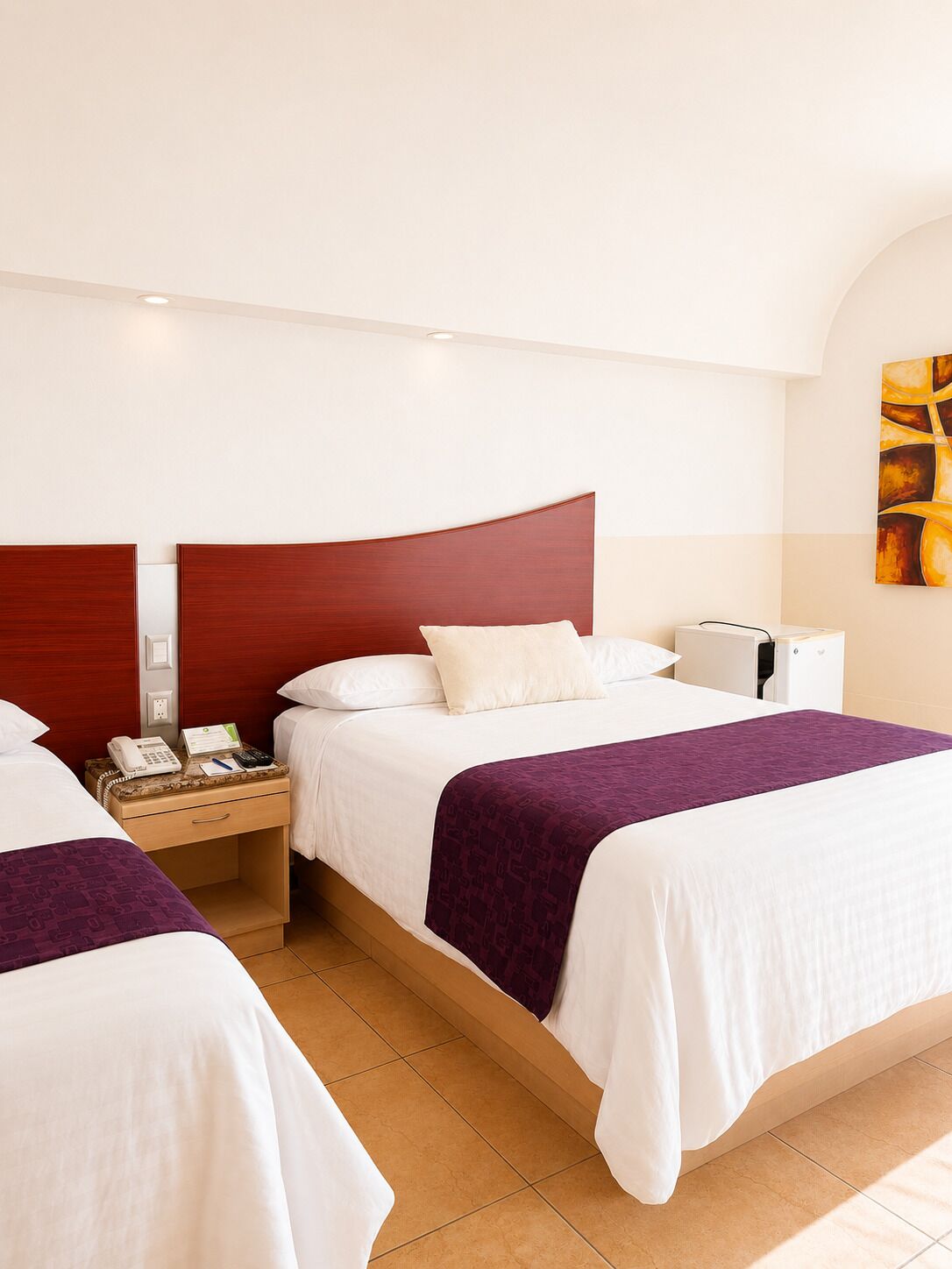 Une chambre d’hôtel avec deux lits, une table de chevet, un téléphone et un tableau au mur.