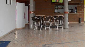 Amplio espacio interior con suelo de baldosas, zona de bar con taburetes y una pantalla de televisión mostrando un evento deportivo.