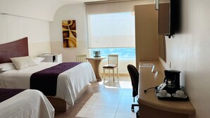 A hotel room with two beds, a desk with a coffee maker, a chair, a TV, and a window with a view.