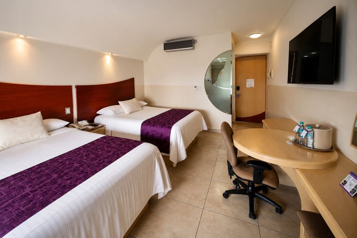 A hotel room with two beds, a desk, a chair, a TV, and a bathroom door.