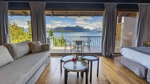 A room with a sofa, a small table with a vase of flowers, and a view of a lake and mountains. - El Faro Boutique Hotel & Spa by DON (Villa La Angostura)
