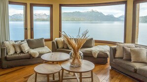 A living room with a view of a lake and mountains. There are two sofas and two round tables. - El Faro Boutique Hotel & Spa by DON (Villa La Angostura)