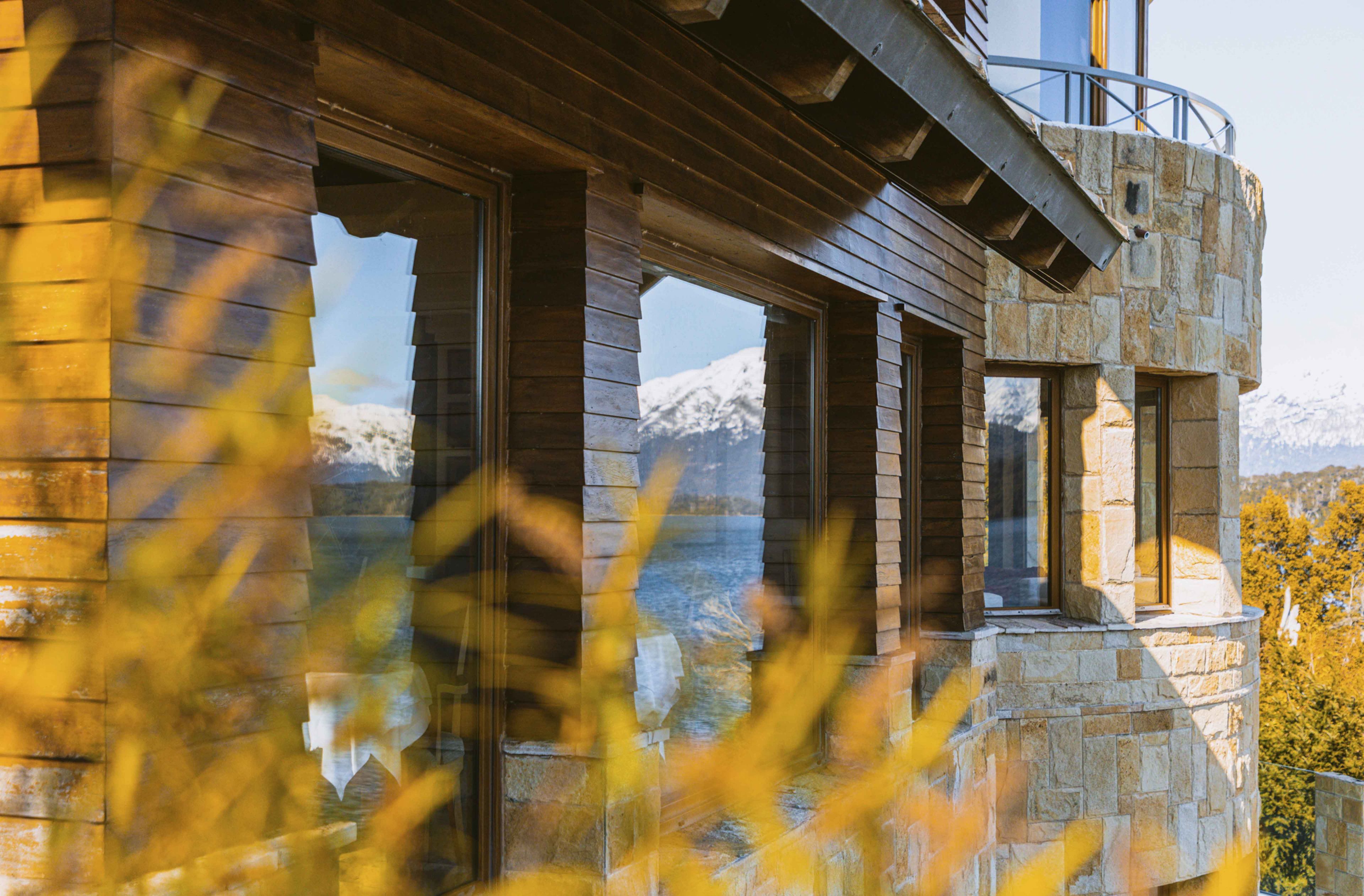 A stone building with large windows and a balcony overlooking a mountainous landscape.